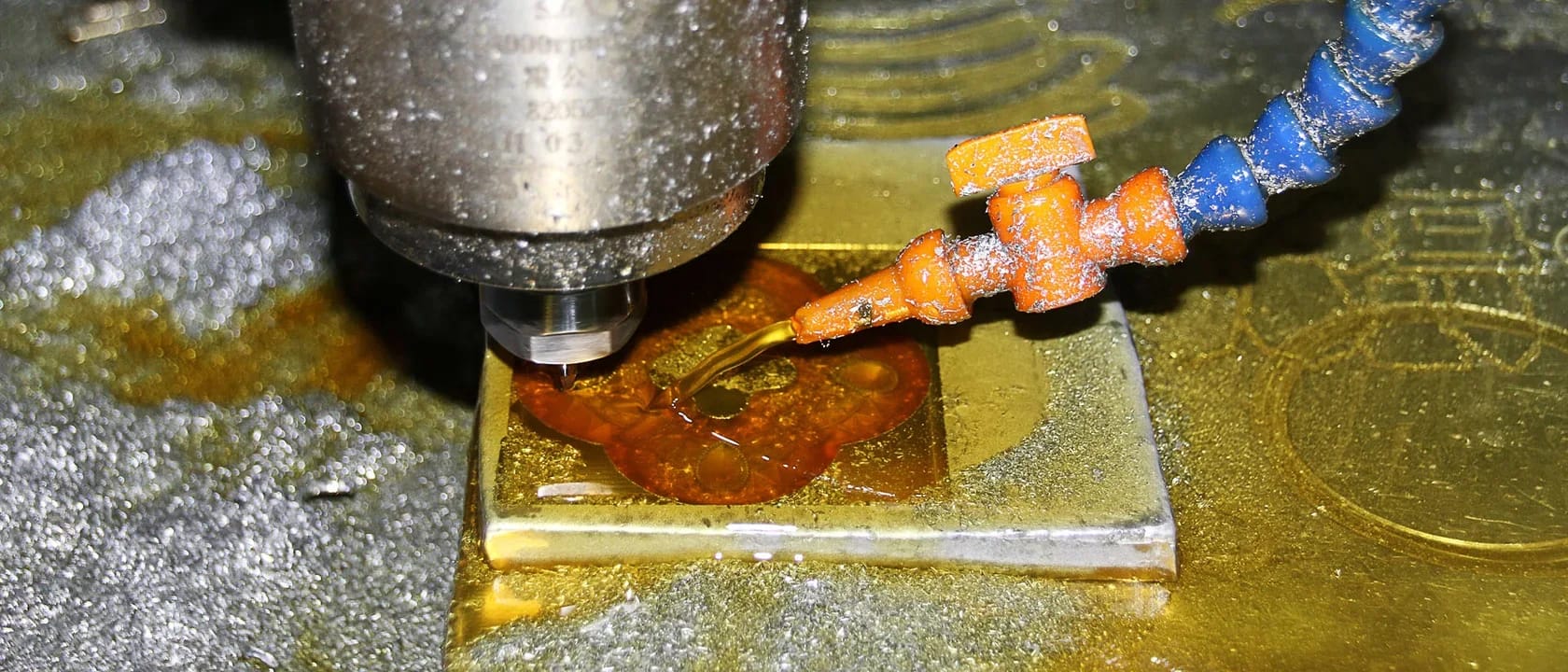 CNC milling spindle and cutting tool above a metal workpiece, with a coolant nozzle beside the tool.