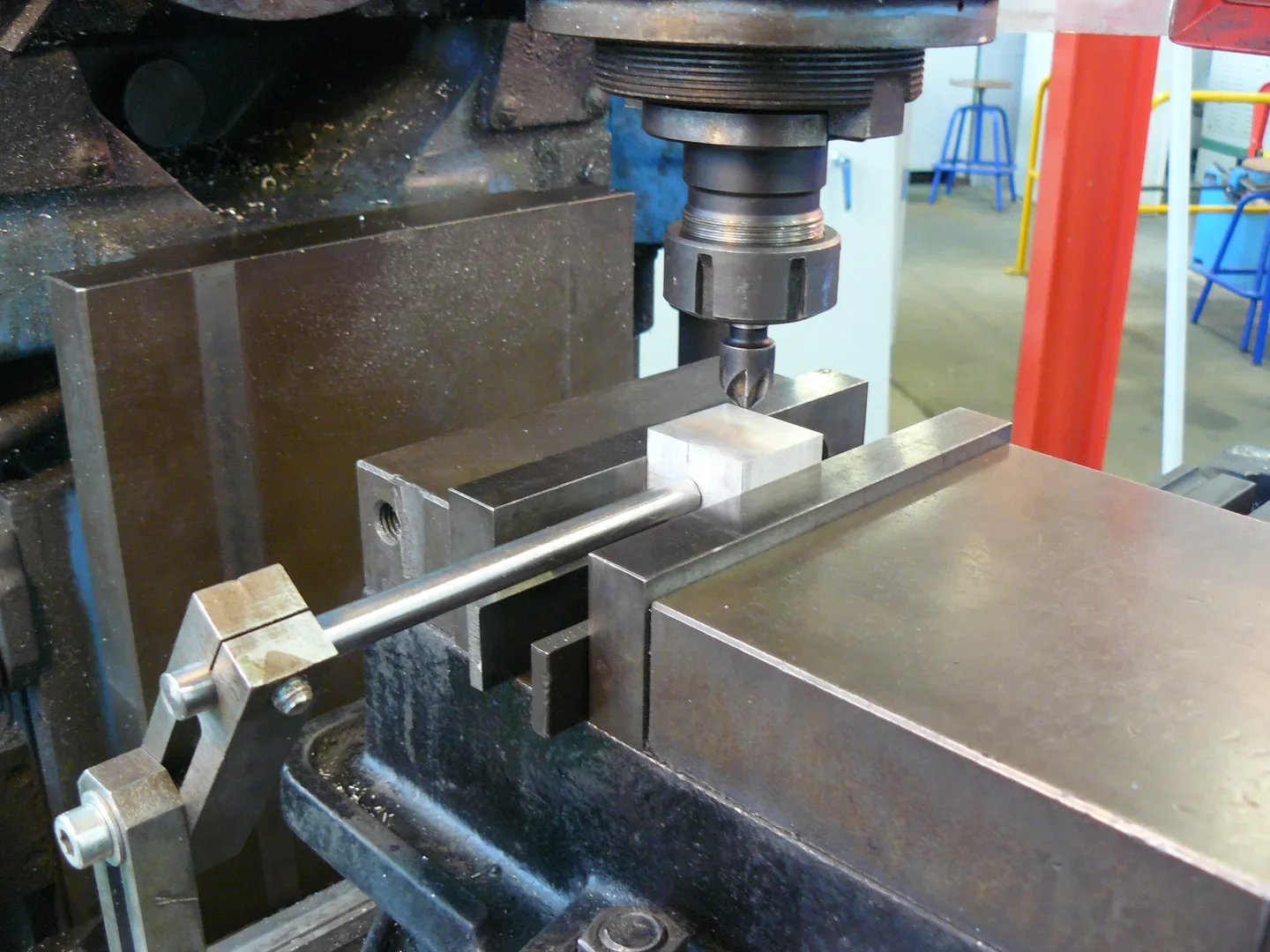 Metal block held in a milling-machine vise, with a stop rod beside the cutter.